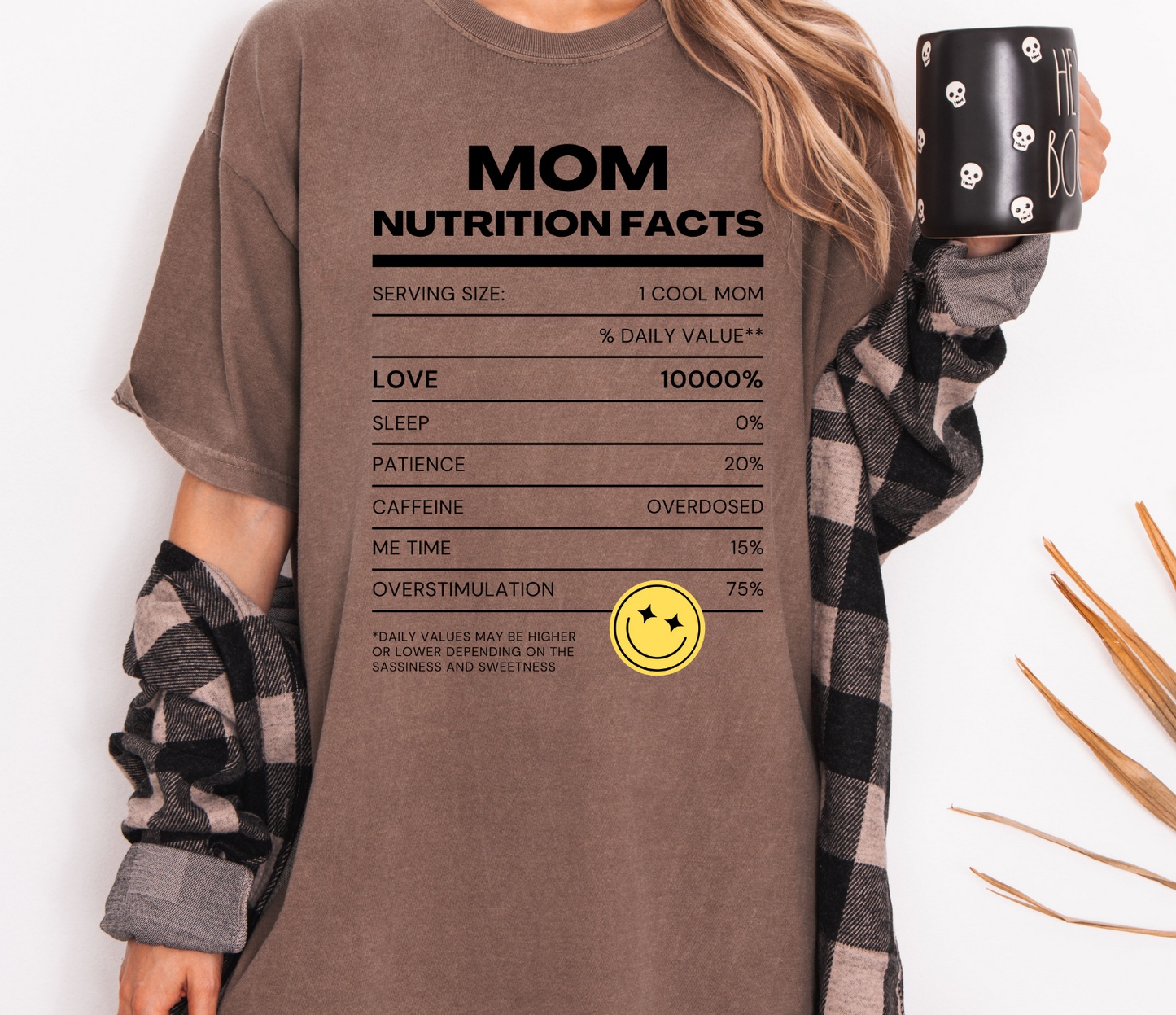 Person wearing a brown t-shirt with 'Mom Nutrition Facts' text and holding a black mug.