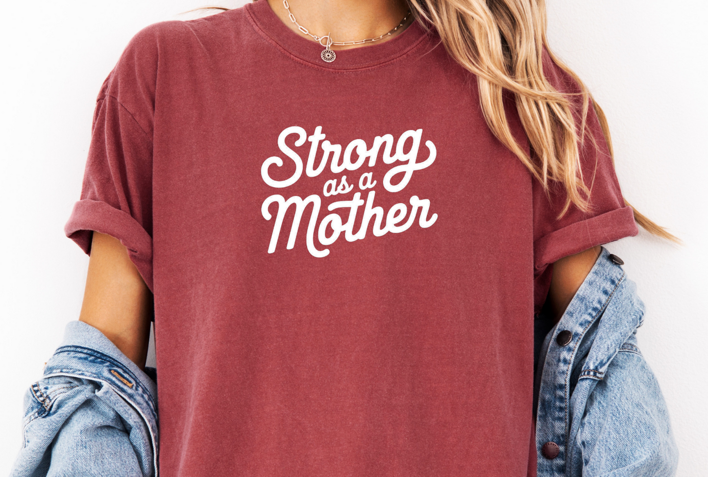 Maroon t-shirt with 'Strong as a Mother' text worn by a person, with a denim jacket over shoulders.